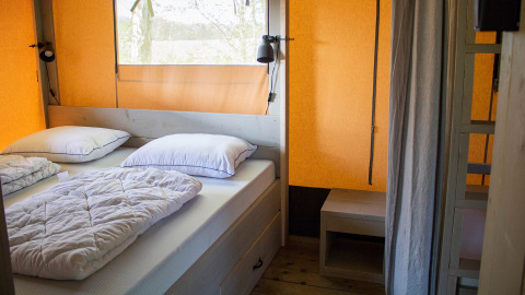 Interior de dormitorio en una tienda safari Villatent Nomad con cama doble, ropa blanca y paredes naranjas.