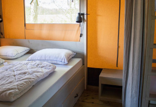Slaapkamer in een Villatent Nomad safaritent met een dubbel bed, witte lakens en oranje wanden.