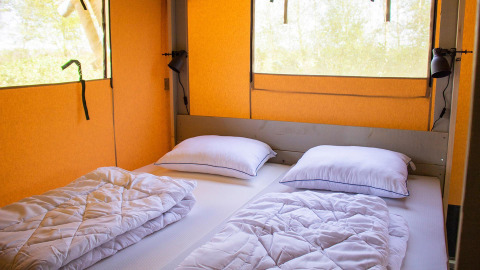 Vista interna di una tenda safari Villatent Nomad con due letti singoli, piumini e cuscini bianchi.