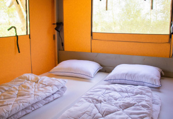 Vista interior de la tienda de safari Villatent Nomad con dos camas, almohadas y luz natural en las ventanas.