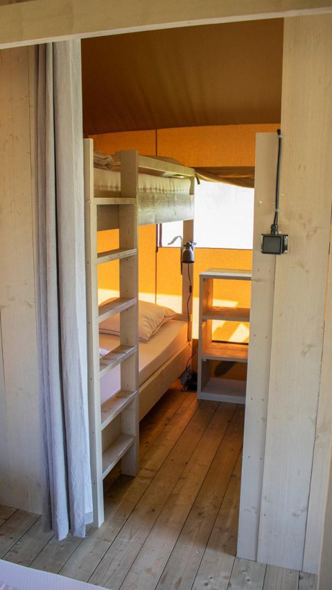 Binnenzicht van Villatent Nomad safaritent met stapelbed, houten vloer en zonlicht door het raam.
