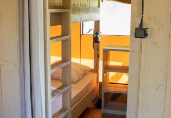 Innenraum eines Villatent Nomad Safari-Zeltes mit Etagenbett, Holzboden und Regal, durch Tür gesehen.
