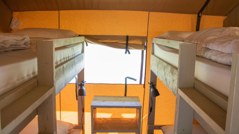 Interior de tienda safari Villatent Nomad con dos literas, muebles de madera y luz natural desde la ventana.