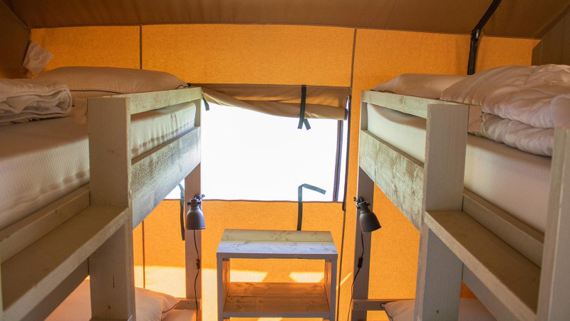 Innenansicht des Villatent Nomad Safarizeltes mit zwei Etagenbetten, Holzmöbeln und natürlichem Licht.