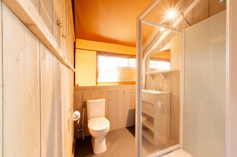 Baño interior de una tienda safari Villatent Nomad con ducha, inodoro y lavabo con estantes almacenaje.