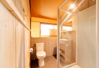 Bagno interno di una tenda safari Villatent Nomad con doccia, WC e lavandino con ripiani portaoggetti.
