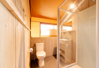 Baño interior de una tienda safari Villatent Nomad con ducha, inodoro y lavabo con estantes almacenaje.