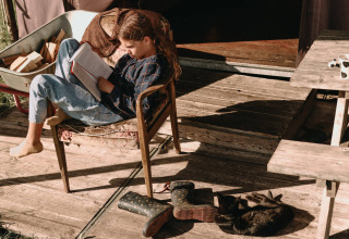 Meisje leest op houten terras met kat en laarzen bij Feather Down Hoeve De Pippert, Gelderland, Nederland.