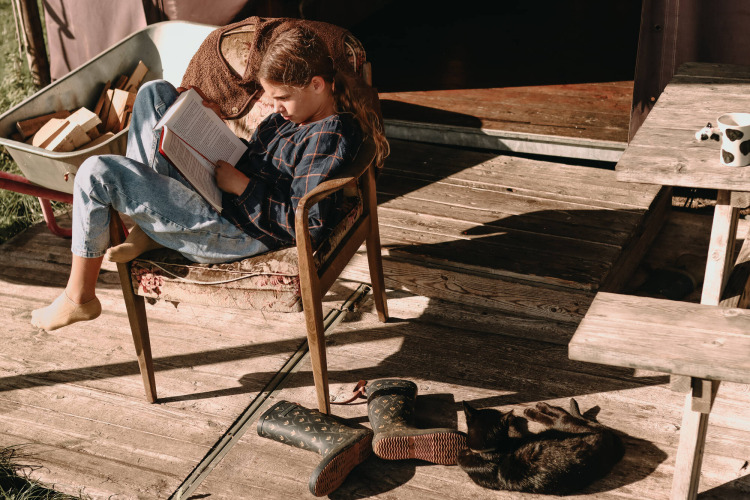 Girl reading book on wooden terrace with a cat and boots at Feather Down Hoeve De Pippert, Gelderland.