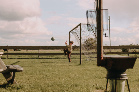 Kind spielt Fußball im Garten mit Tor, Wiese und Feldern bei Ophemert, Gelderland, Niederlande.