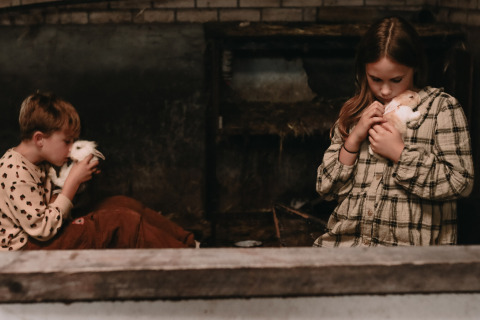 Two children cuddle rabbits in a rustic barn at Feather Down Hoeve De Pippert, Gelderland, Netherlands.