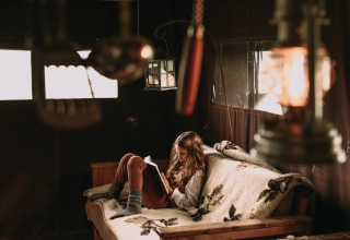 Ein Mädchen liest ein Buch auf einem Sofa mit Decke in einer gemütlichen, schwach beleuchteten Hütte.