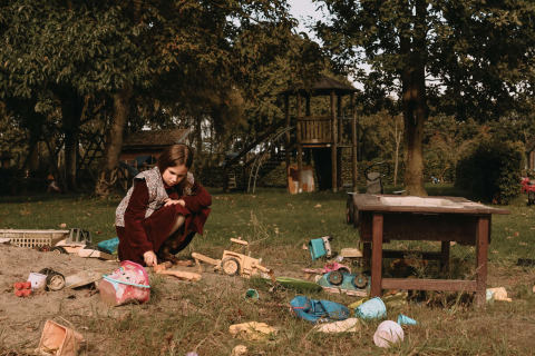A girl playing with toys in a sandbox on a playground surrounded by greenery near Ophemert, Netherlands.