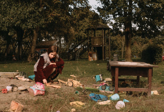 A girl playing with toys in a sandbox on a playground surrounded by greenery near Ophemert, Netherlands.
