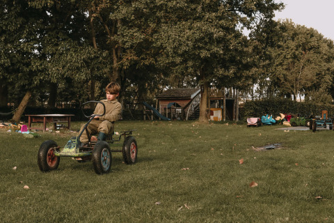 Un niño conduce un coche de pedales en un parque de juegos rodeado de árboles y juguetes en Gelderland, Países Bajos.