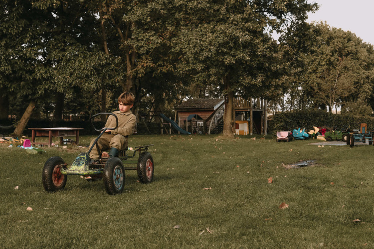Ein Kind fährt ein Tretauto auf einem Spielplatz, umgeben von Bäumen und Spielzeug in Gelderland, Niederlande.