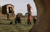Two people with goats and chickens near a treehouse on a grassy field in Ophemert, Gelderland, Netherlands.