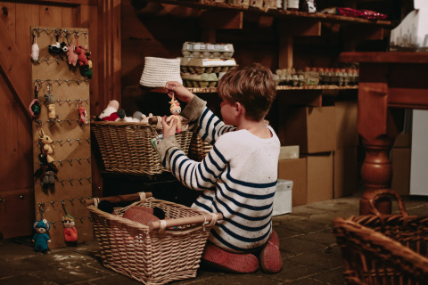 Un enfant en pull rayé regarde des porte-clés crochetés dans une boutique de Hoeve De Pippert, Pays-Bas.