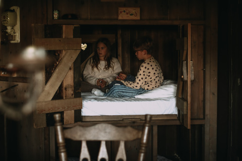 Zwei Kinder sitzen und unterhalten sich auf einem Bett in einer rustikalen Holzhütte im Feather Down Hoeve De Pippert.