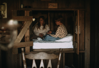 Twee kinderen zitten te praten op een bed in een gezellige houten hut bij Feather Down Hoeve De Pippert, Gelderland.