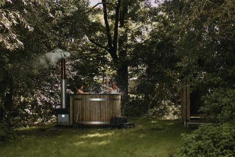 Dos personas disfrutan de un jacuzzi al aire libre entre árboles en Feather Down Hoeve De Pippert, Países Bajos.