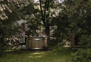 Twee personen ontspannen in een houten hot tub tussen de bomen bij Feather Down Hoeve De Pippert, Betuwe.