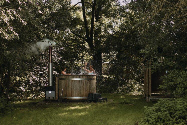 Two people enjoy a hot tub outdoors surrounded by trees at Feather Down Hoeve De Pippert in Gelderland.