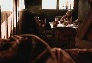 Vrouw zit aan tafel in zonnig verlichte hut bij Feather Down Hoeve De Pippert, vakantiepark Gelderland.