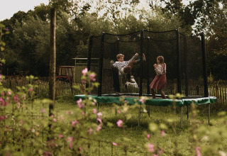To børn leger på en trampolin i en have med blomster ved Feather Down Hoeve De Pippert, Gelderland, Holland.