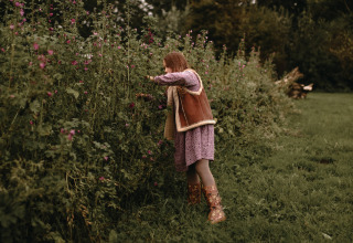 Et barn i lilla kjole og støvler plukker blomster i en blomstrende have i Feather Down Hoeve De Pippert.
