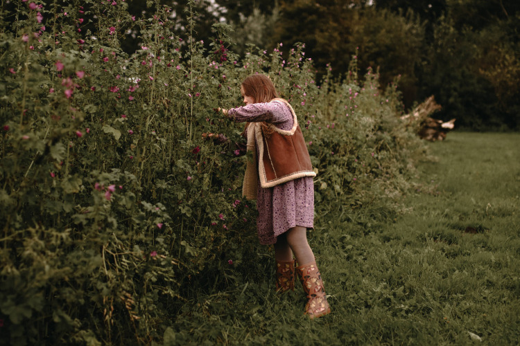 A child in a purple dress and boots picks flowers in a lush garden at Feather Down Hoeve De Pippert.