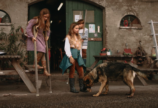 Børn leger med en hund foran en rustik bygning i ferieparken Hoeve De Pippert i Gelderland, Holland.