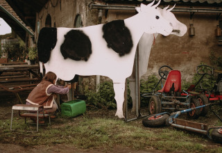 Child milking an artificial cow at Feather Down Hoeve De Pippert, holiday park in Gelderland, Netherlands.