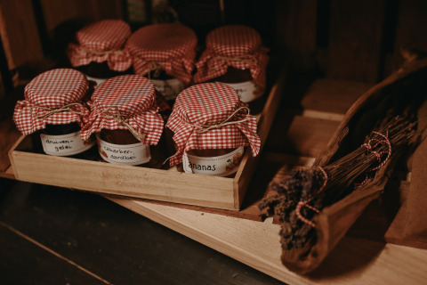 Hausgemachte Marmeladengläser mit rotweiß karierten Deckeln auf einem Holztablett bei Feather Down Hoeve De Pippert.