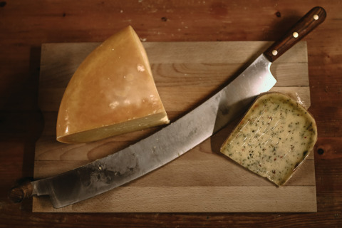 Cuchillo grande y dos trozos de queso en tabla de madera en Feather Down Hoeve De Pippert, Gelderland, Países Bajos.