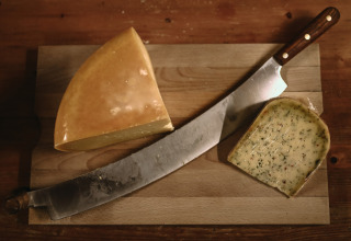 Cuchillo grande y dos trozos de queso en tabla de madera en Feather Down Hoeve De Pippert, Gelderland, Países Bajos.