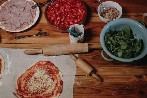 Preparando pizza con jamón, espinacas, tomates y más ingredientes en una mesa de madera en un parque vacacional.