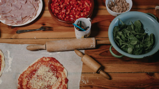 Preparando pizza con jamón, espinacas, tomates y más ingredientes en una mesa de madera en un parque vacacional.
