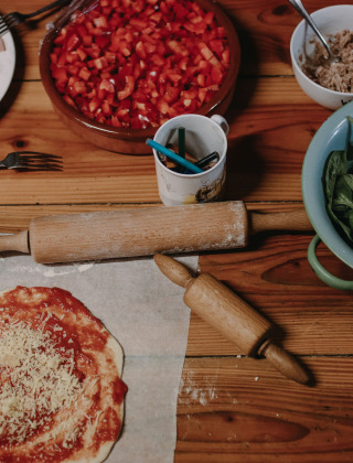 Preparando pizza con jamón, espinacas, tomates y más ingredientes en una mesa de madera en un parque vacacional.