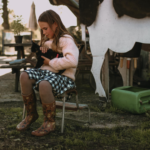 Fille en robe à carreaux et bottes caresse un chat noir à Hoeve De Pippert, Gelderland, Pays-Bas.