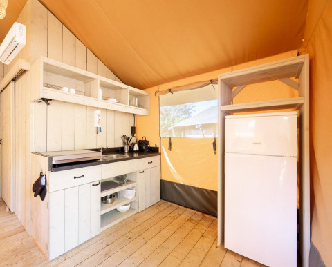 Zona de cocina en una tienda safari Villatent Nomad, con frigorífico, estanterías y suelos de madera.