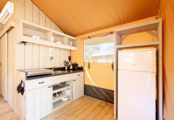 Angolo cucina in una tenda safari Villatent Nomad con frigorifero, scaffali a giorno e pavimento in legno.