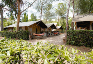 Tienda safari Villatent Nomad en Camping Casa dei Prati en Italia, rodeada de árboles, hamacas y vegetación.