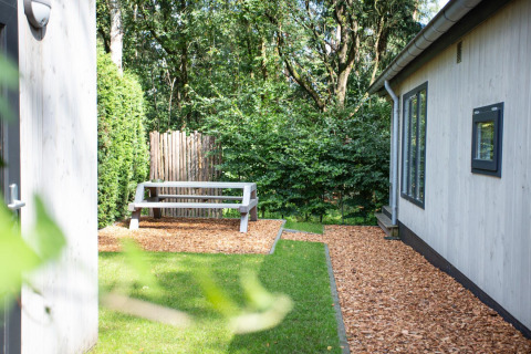 Buitenomgeving van Boslodge op De Thijmse Berg in Nederland, met zitbank, houtsnippers en veel groen.