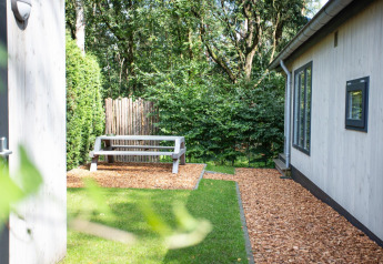 Udendørs område ved Boslodge på De Thijmse Berg i Holland med bænk, træflis og grøn beplantning.