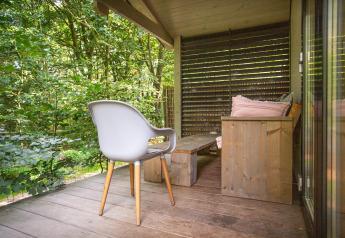 Træveranda ved Boslodge De Thijmse Berg i Holland med moderne stol, bænk og udsigt til skov.