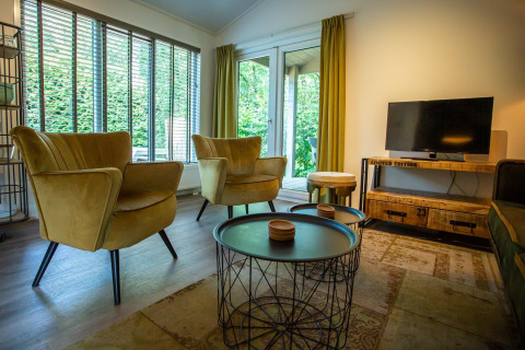 Sala de estar en Boslodge en De Thijmse Berg, Países Bajos, con muebles modernos, grandes ventanales y TV.