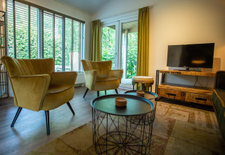 Sala de estar en Boslodge en De Thijmse Berg, Países Bajos, con muebles modernos, grandes ventanales y TV.