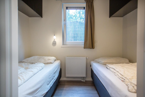 Dormitorio en Boslodge de De Thijmse Berg, Países Bajos, con dos camas individuales, ventana y decoración moderna.