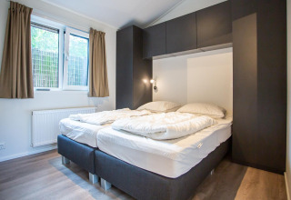 Dormitorio moderno con dos camas, grandes ventanas y armarios en Boslodge, De Thijmse Berg, en los Países Bajos.